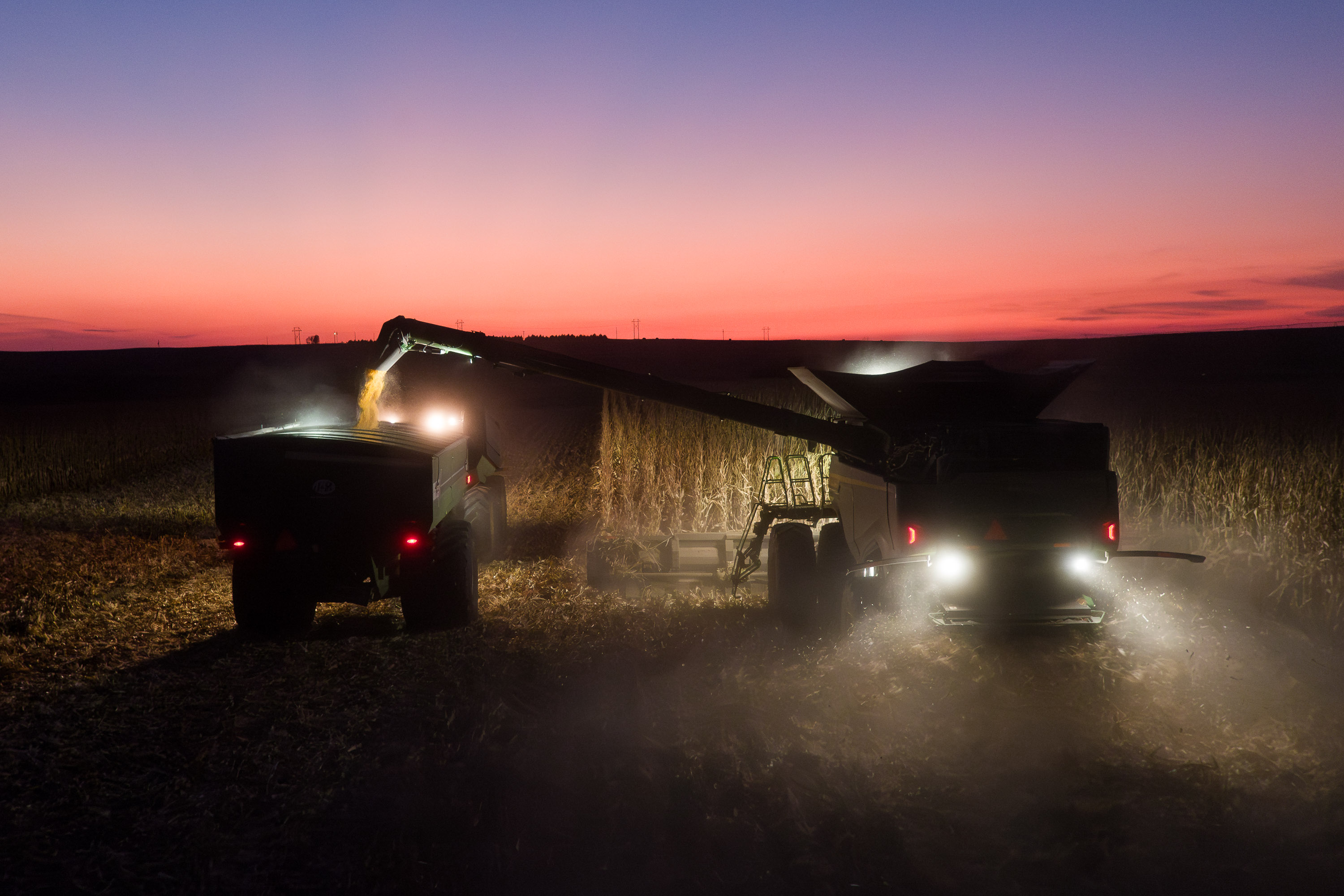 harvest photo with John Deere Tracker with grain cart and combine at sunset